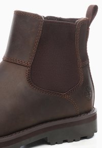 Bota Chelsea de cuero marrón con paneles laterales elásticos, costuras en contraste, suela de goma y un logotipo grabado en el lateral.