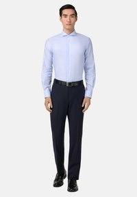 Lichtblauw overhemd met lange mouwen, een kraag, knoopsluiting aan de voorkant en een aansluitende pasvorm, gecombineerd met marineblauwe pantalon en zwarte schoenen.