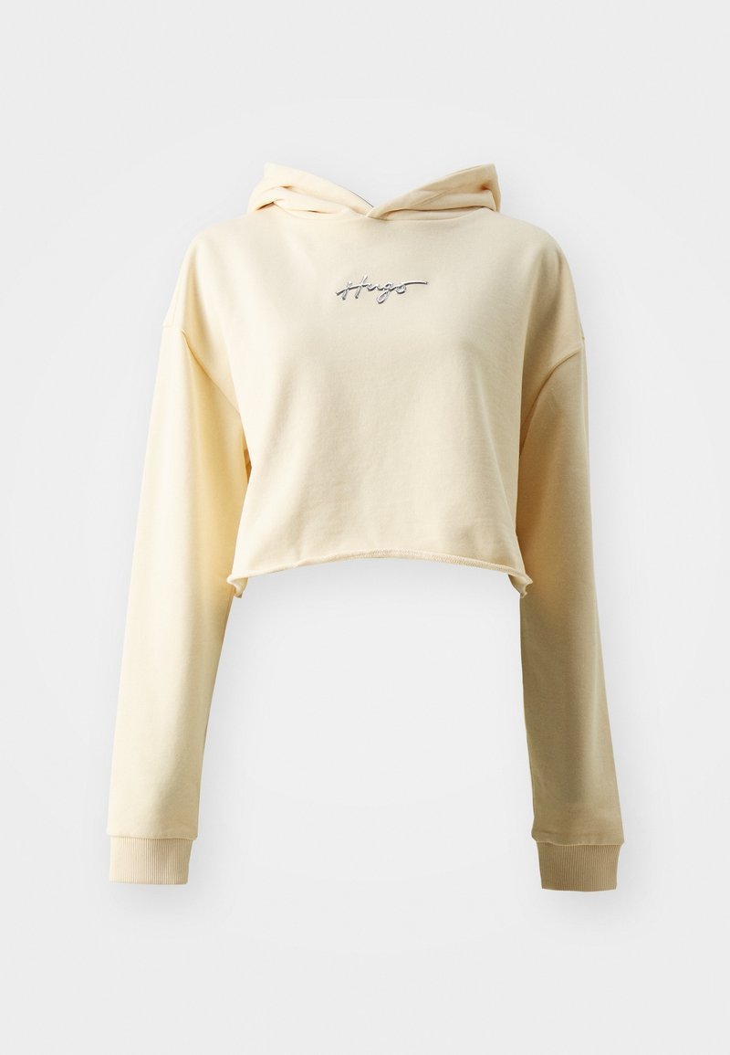 Sweat à capuche court crème avec manches longues et petit logo "Hugo" argenté centré sur la poitrine, sur un fond uni.