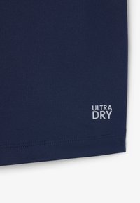 Tessuto blu scuro con la scritta "ULTRA DRY" in bianco vicino all'orlo cucito nell'angolo inferiore.