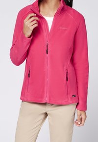 Fleece jacket in bright pink, featuring a high collar, front zip closure, and zippered side pockets. Textured fabric enhances warmth.
