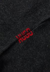 Tissu en tricot noir avec une texture douce, présentant un logo rouge brodé bien visible. Le design est simple et discret.