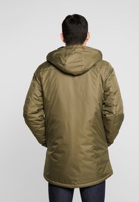 Doudoune vert olive avec capuche, en matière lisse et légère. Présente une coupe mi-longue et des poignets élastiques.