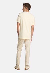 Lys gul bomulds T-shirt med korte ærmer, afslappet pasform. Båret med beige bukser og sneakers i neutrale nuancer, der fremhæver et enkelt design.