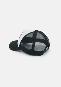 Casquette de camionneur noire et blanche avec panneaux arrière en maille et fermeture à pression réglable, reposant sur le côté sur une surface unie.