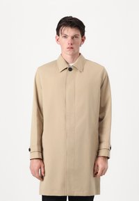 Beige trench coat with a straight design, pointed collar, and button closure. Features long sleeves with buttoned cuffs and side pockets.