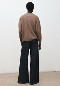 Maglione marrone a maglia con girocollo e spalle scese, abbinato a jeans in denim scuro a gamba larga con tasche posteriori e cuciture in evidenza.