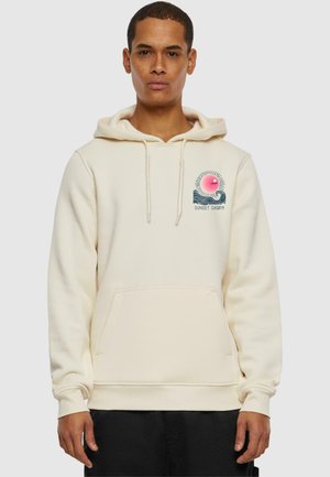 Cremefarbener Hoodie mit Kängurutasche, Kordelzügen und einem grafischen Druck eines Sonnenuntergangs über Wellen. Hergestellt aus weichem Stoff, mit gerippten Bündchen.