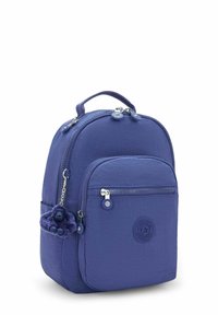 Sac à dos en nylon violet de forme arrondie, avec fermetures éclair et une poche avant. Comprend un pendentif texturé et un détail de logo sur le côté.