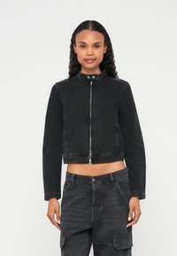 Κοντό μαύρο τζιν μπουφάν με ψηλό γιακά, κλείσιμο με φερμουάρ και μακριά μανίκια. Λεπτή υφή με ελάχιστα μεταλλικά στοιχεία και εφαρμοστή σχεδίαση.