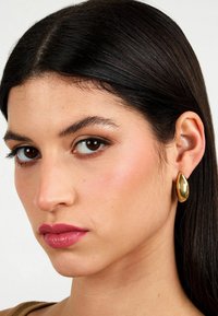 Orecchini ovali in oro realizzati in metallo lucido, caratterizzati da una texture liscia e una leggera lucentezza, progettati per adattarsi comodamente all'orecchio.