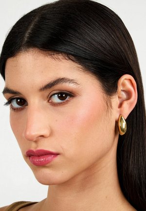 Orecchini ovali in oro realizzati in metallo lucido, caratterizzati da una texture liscia e una leggera lucentezza, progettati per adattarsi comodamente all'orecchio.