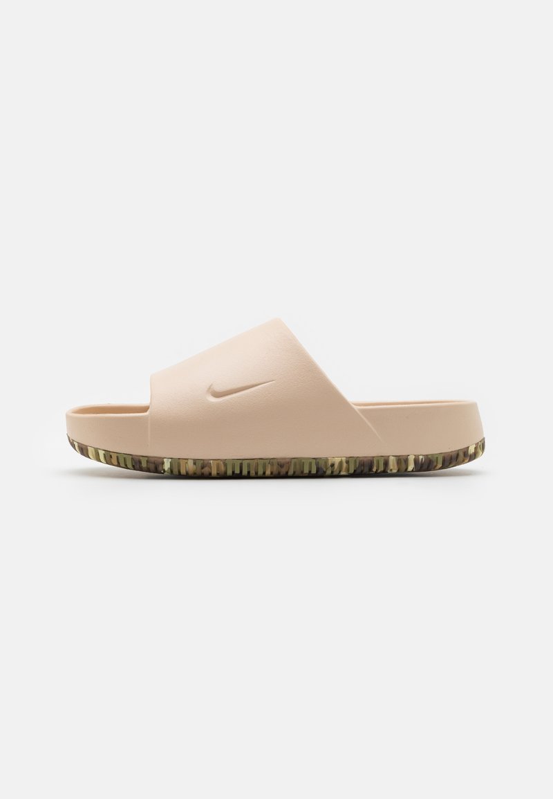 Nike slide sandal in light peach color, featuring a wide strap, textured footbed, and a patterned dark green sole with a camouflage design.