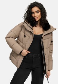 Beige pufferjack met een afneembare zwarte faux fur kraag, ritssluiting en een gestikt patroon. Gepaard met een zwarte top en hoge taille jeans.