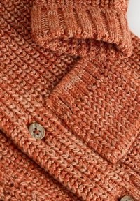 Pletena cardigan v različnih odtenkih oranžne in bež, ki vključuje rebrast ovratnik, zapiranje na gumb in strukturiran vzorec.