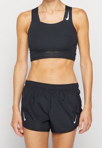 Černá sportovní podprsenka s texturovaným designem a výřezy, doplněná černými šortkami s elastickým pasem a logem.