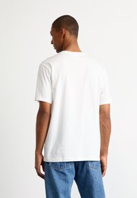 Maglietta bianca in cotone con scollatura a girocollo e maniche corte, vista da dietro. Presenta una vestibilità comoda e una superficie liscia.