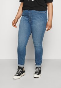 Chude niebieskie dżinsy z wysokim stanem, z zamkiem błyskawicznym i podwiniętymi mankietami. W połączeniu z czarnymi sneakersami za kostkę i czarnym t-shirtem.