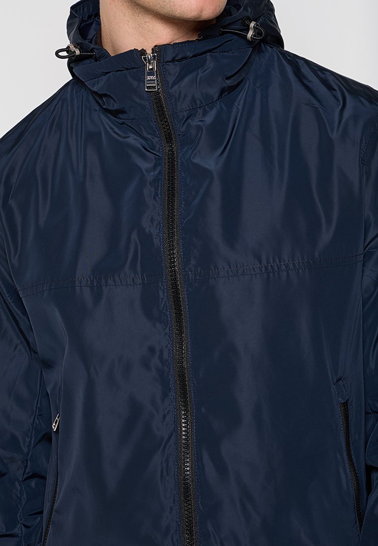 Dunkelblaues, leichtes Jacket mit glatter, glänzender Oberfläche, Reißverschluss vorne und Kapuze. Mit Kordelzügen und seitlichen Taschen.