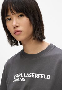 Camiseta gris de cuello redondo con el logotipo en texto blanco "KARL LAGERFELD JEANS" en el pecho. Tejido de algodón suave con un corte relajado.