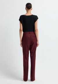 Zwart T-shirt met korte mouwen, gecombineerd met hoogoplopende, bordeauxrode broeken met een getailleerde pasvorm en subtiele achterzakdetails.