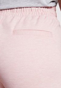 Lichtroze sweatpants van een gestructureerde stof, met een elastische tailleband en een klein achterzakje. Eenvoudig ontwerp, geen zichtbare patronen.