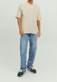 Beige korte mouwen overhemd met een textuurpatroon, knoopsluiting aan de voorkant, gecombineerd met lichtblauwe jeans en groene sneakers met witte accenten.