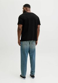 Camiseta de algodón negra de manga corta, combinada con jeans de pierna ancha de color azul claro, ligeramente desgastados, y zapatillas negras con suelas blancas.