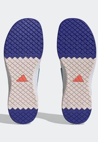 Semelles de chaussures de sport blanches et bleues avec des motifs texturés ; caoutchouc bleu au bout et logo orange Adidas sur fond blanc.