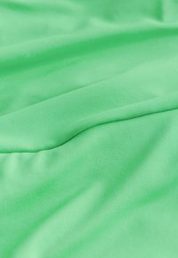 Grönt tyg med en slät, elastisk textur. Materialet verkar lätt och är vikt med mjuka vågor, vilket visar en jämn färg genom hela ytan.