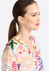 Colorful, patterned blouse with a v-neck design. Features sun, heart, and palm motifs in pink, green, orange, and blue on a soft pink background.