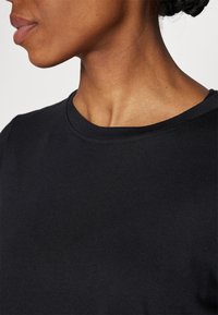 Schwarzes Baumwoll-T-Shirt mit Rundhalsausschnitt, glatter Textur und kurzen Ärmeln, das minimale Nähdetails zeigt.