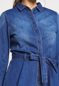 Denim jurk met een kraag, knopen aan de voorkant en een strikceintuur op de taille. Kenmerkt zich door een gestructureerde blauwe stof met een gladde afwerking.