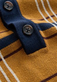 Strikket sweater med struktur i sennepsgul med marineblå detaljer. Har to mørke knapper og horisontale striber i hvid og burgunder.
