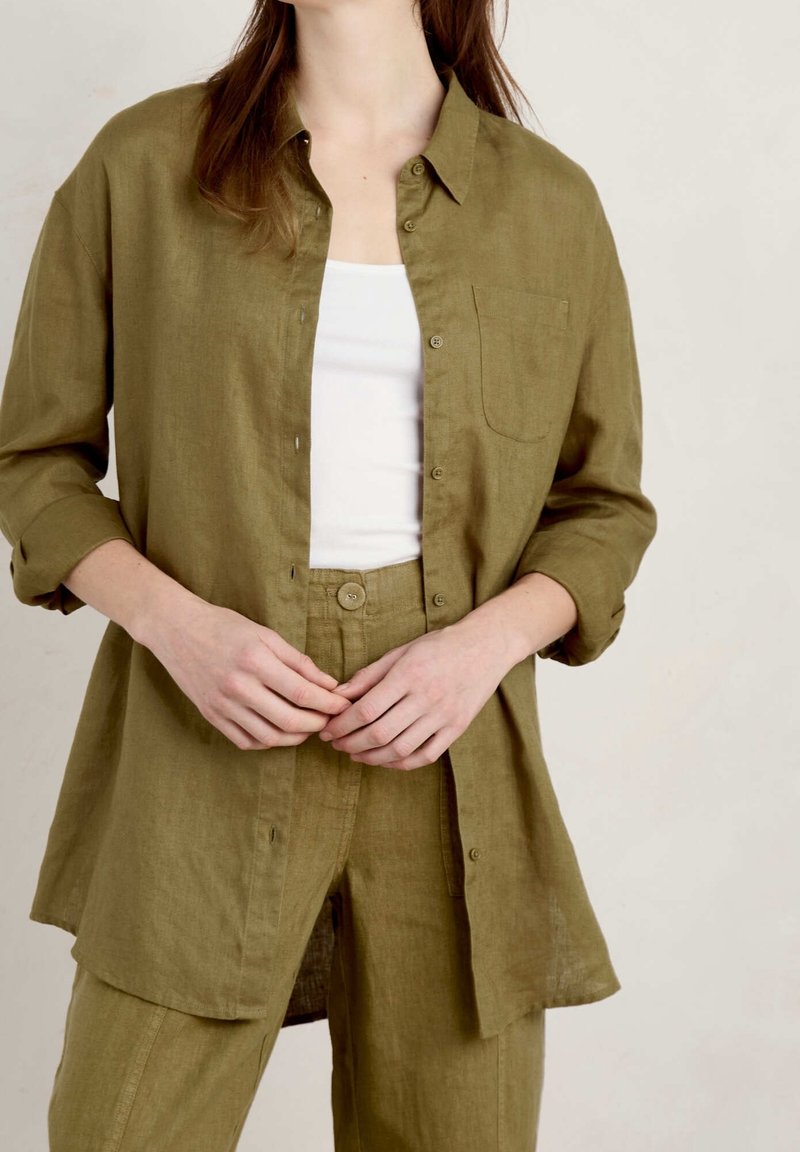 Olive green linen shirt with long sleeves, button-down front, and a chest pocket, styled with matching high-waisted pants. Smooth texture.