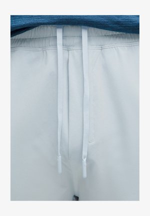 Bele športne hlače z elastičnim pasom in vrvico; gladka tekstura; dve sprednji žepi z minimalnimi šivi.