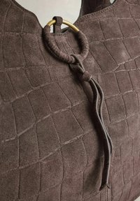 Prillitäpsusega pruunast seemisnahast käekott, millel on tikitud muster ja kuldne metallrõngas, mis on kinnitatud nahast rihmale.