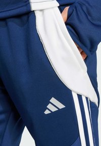Marineblaue Sporthosen mit einem weißen Seitenpanel, drei weißen Streifen und einem grauen adidas-Logo am Oberschenkel. Glatte Textur, sportliches Design.