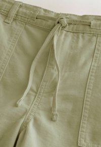 Gros plan sur un pantalon beige avec un cordon en tissu noué à la taille et des détails de couture visibles.