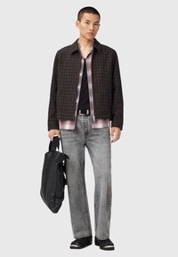 Tenue masculine comprenant une veste à motif carreaux foncés, une chemise à carreaux grise, un t-shirt noir, un jean gris et un sac à bandoulière noir.