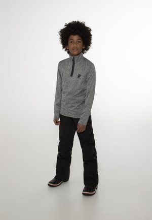 Grijze, lange mouwen ritssluittop met hoge kraag en logo, gecombineerd met zwarte broek en zwarte laarzen met rode accenten. Over het geheel een gladde textuur.