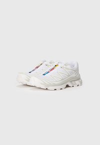Zapatillas deportivas blancas con parte superior de malla, puntera reforzada, suela texturizada y marcas coloridas en los cordones. Diseño ligero y transpirable.