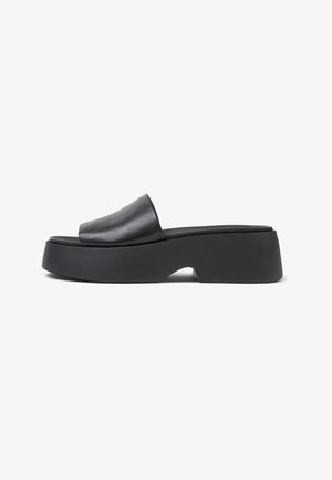 Černé skládací boty s elegantním koženým svrškem. Obsahují tlustou platformu s zakřiveným výřezem, což zvýrazňuje moderní design.