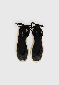 Scarpe in stile espadrillas nere con tomaia in rete, punta rotonda e suola intrecciata beige. Presentano lacci in tessuto nero per la chiusura.