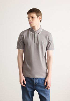 Graues Polohemd mit klassischem Kragen, Knopfleiste und kontrastierenden weißen Akzenten. Verfügt über ein kleines Logo-Patch auf der linken Seite.