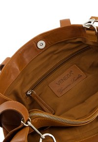 Brauner Lederhandtaschen-Innenraum mit einem Reißverschlussfach, Stoffauskleidung, Logopatch, Druckknopfverschluss und silbernen Hardware-Akzenten.