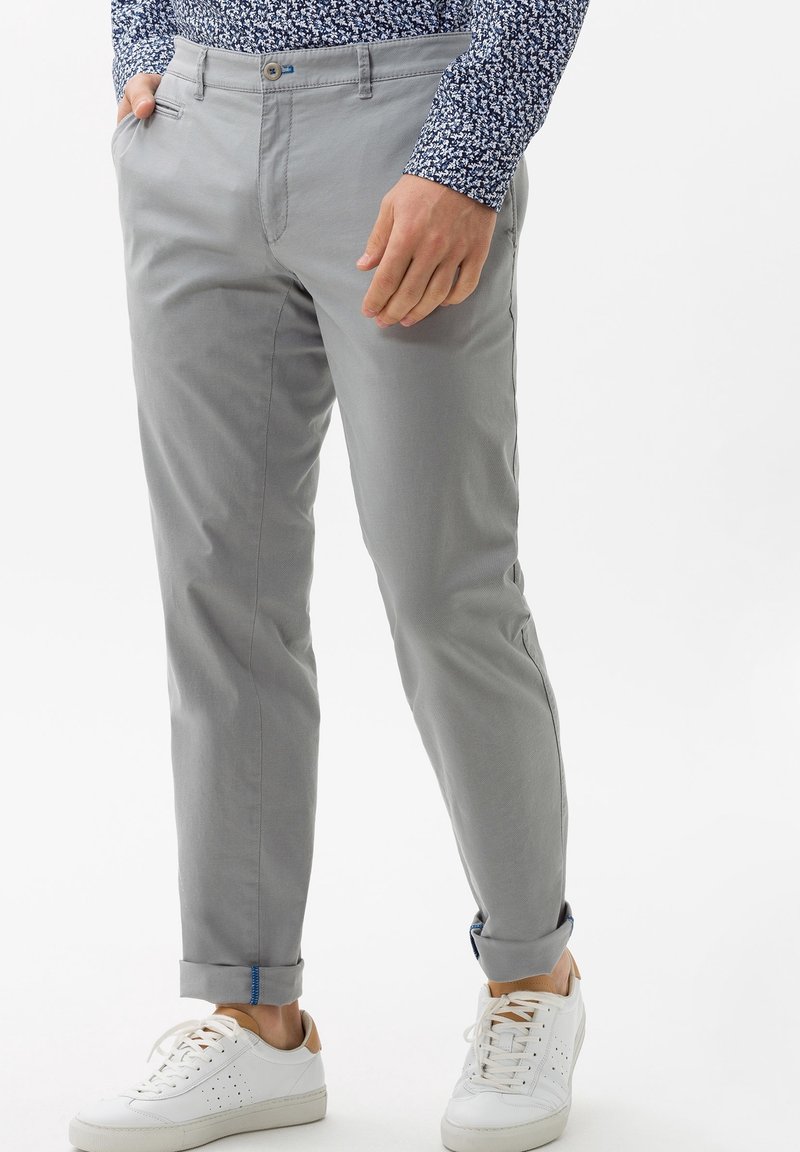 Pantaloni di cotone grigi con vestibilità slim, caratterizzati da un orlo arrotolato, tasche anteriori e chiusura con bottone, abbinati a sneakers bianche.