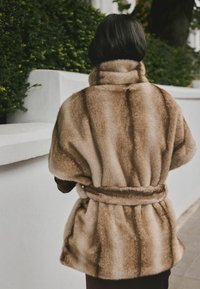 Faux fur wrap with a high collar and belted waist. Features a light brown color with darker stripes and a soft, plush texture.