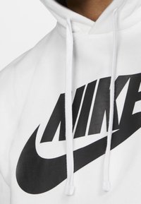 Hoodie blanc avec un logo Nike noir bien en vue, doté d'une texture douce et de cordons de serrage ajustables. Vue rapprochée du tissu et du design.