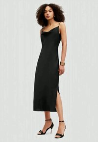 Vestido midi de satin preto com decote drapeado, alças finas e fenda lateral. Modelo usa sandálias pretas de tiras e uma pulseira metálica.